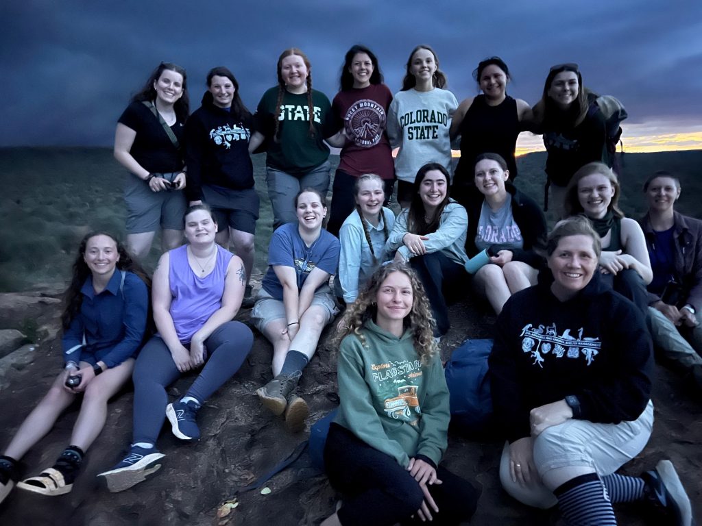 A group of C S U students pose for a group photo, along with their professor Jennie Willis, while out in the plains at sunset.