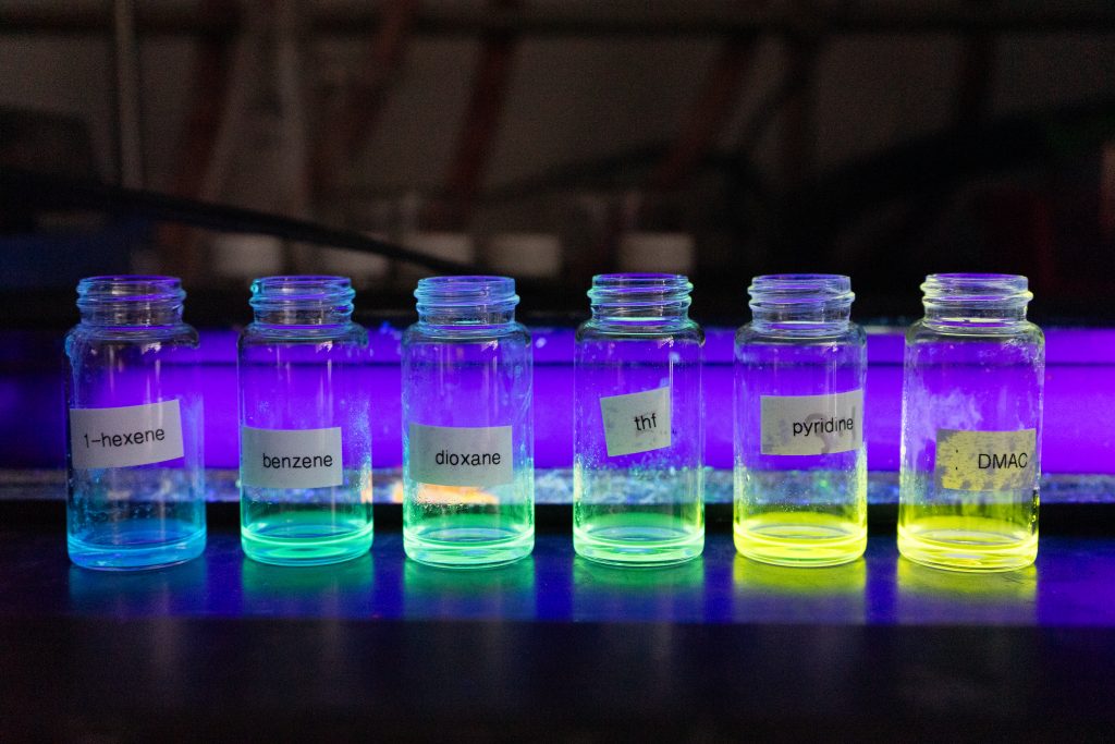 Vials, illuminated by a blacklight, sit in a line and are glowing with colored liquid. 