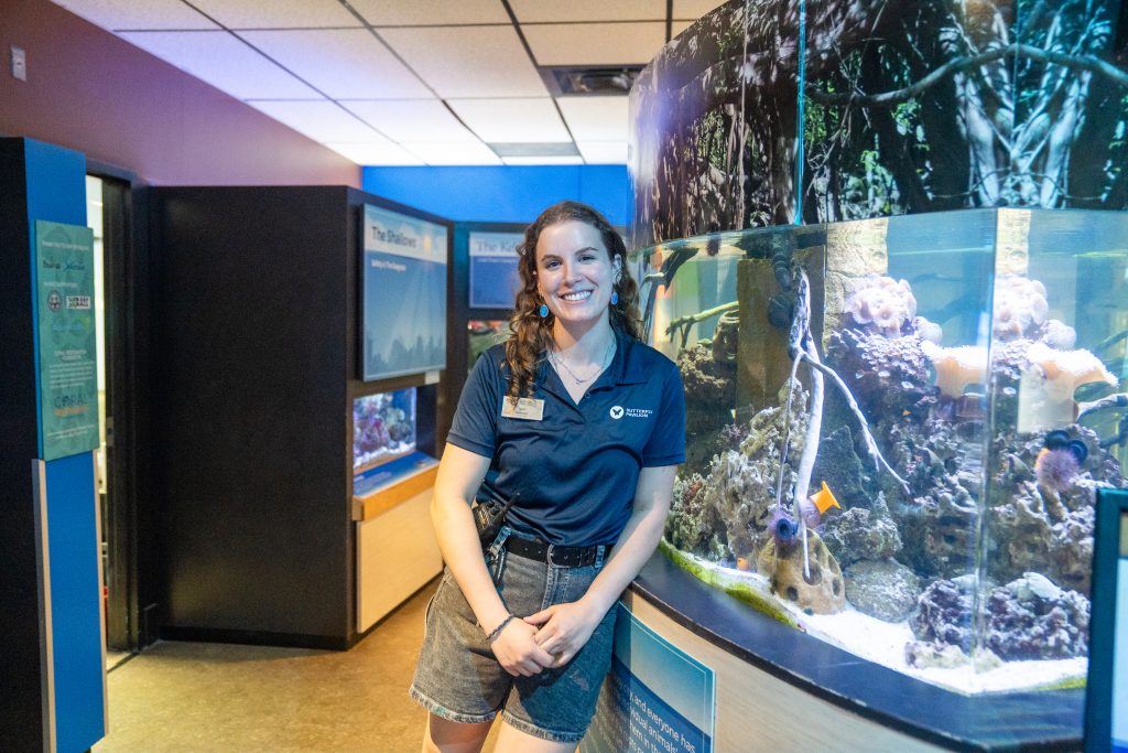 A female student stands smiling next to a fish tank.